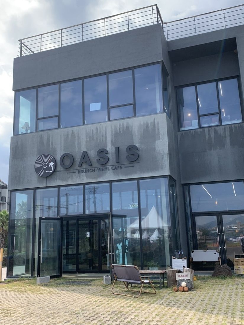 오아시스 제주 — 바다를 등지고 선 3층 규모의 검은색 건물 외관